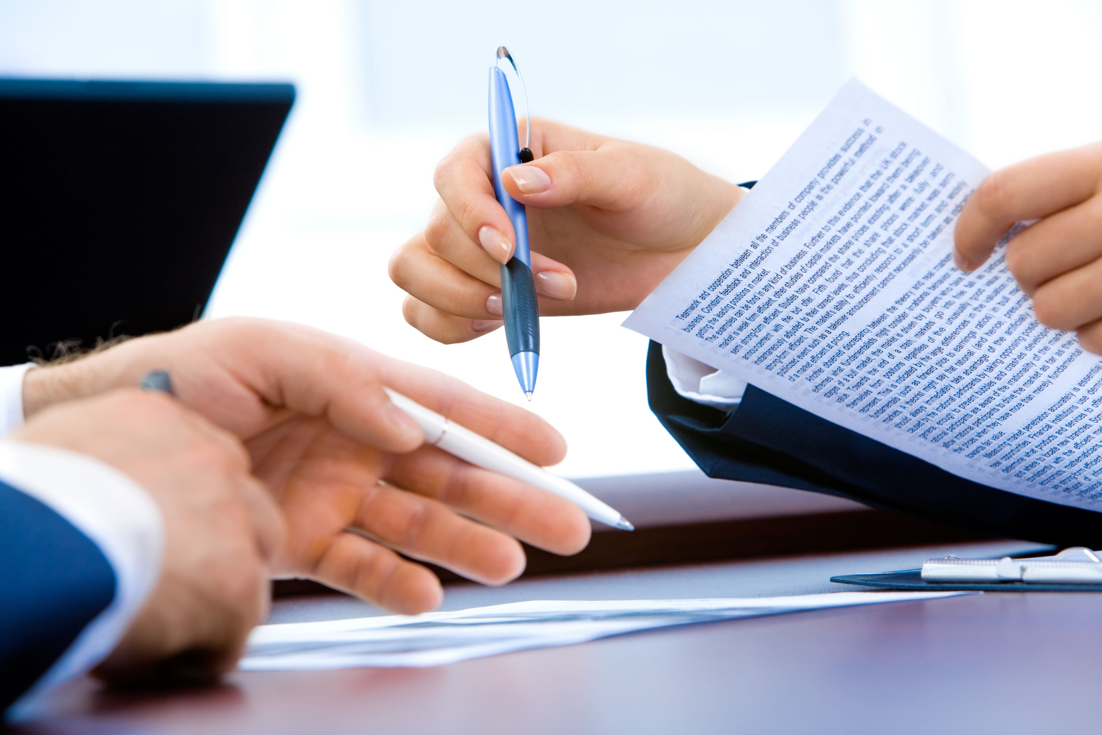 two people hands one holding paper and pen, other person writing and holding a pen