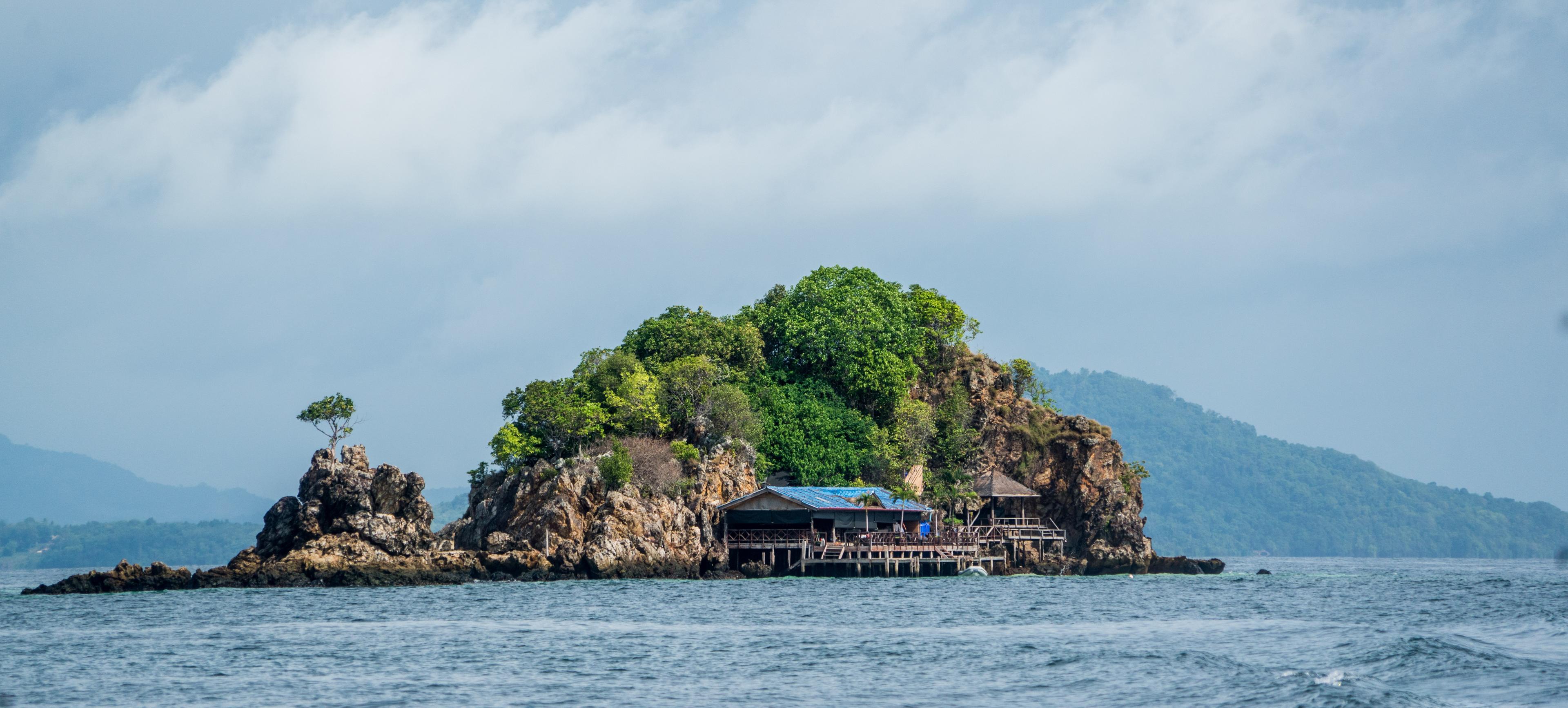 A traditional long-tail boat is anchored on the pristine shores of Phuket, Thailand. The boat’s wooden hull is painted in vibrant colors, with the bow adorned with brightly colored ribbons and garlands, symbolizing good luck.